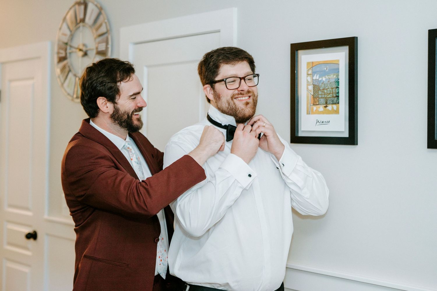 Two people getting ready for a wedding ceremony, sharing a candid moment in a bright indoor room.