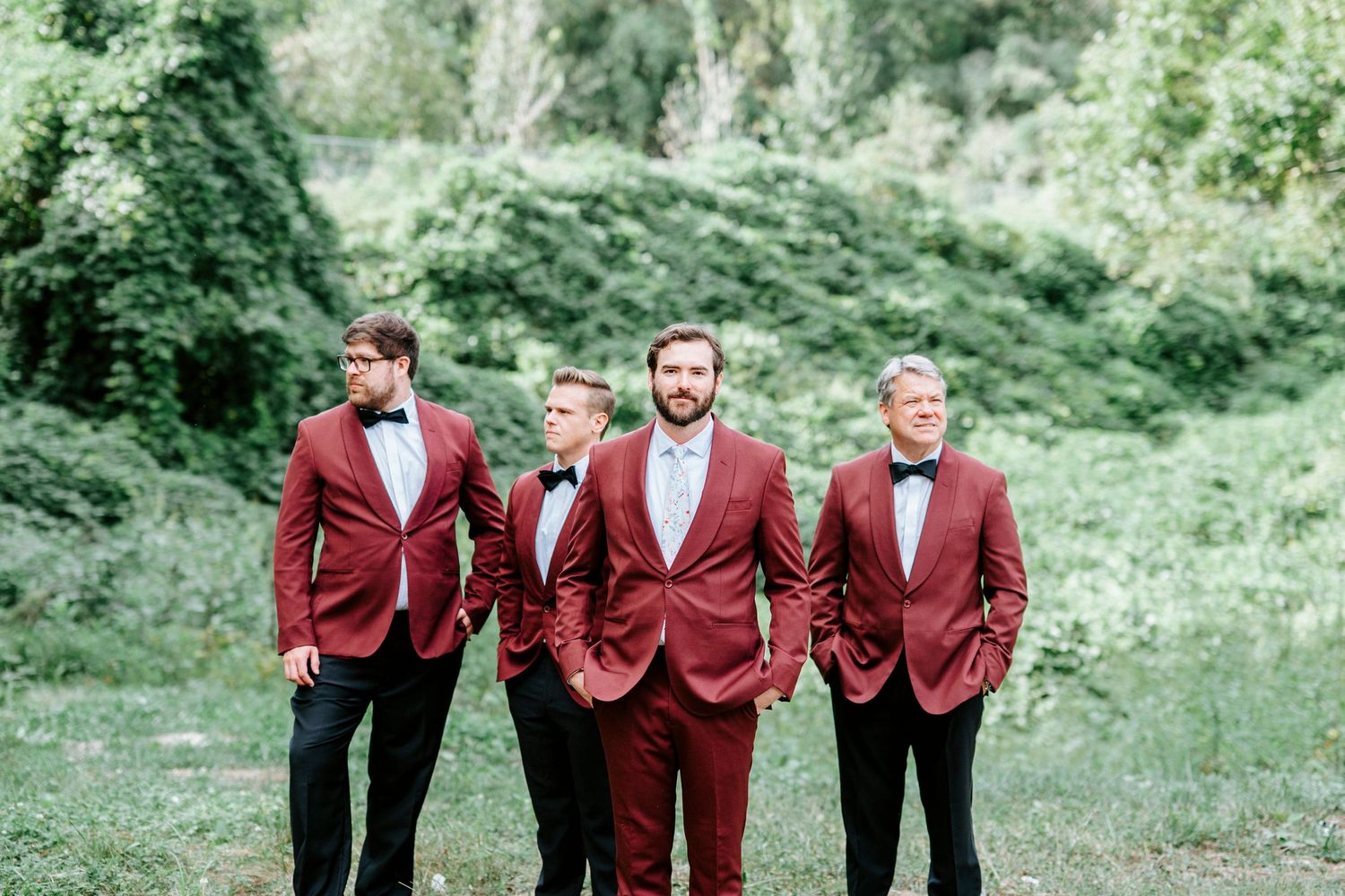 A festive group in matching burgundy formal jackets poses together in an outdoor garden setting.