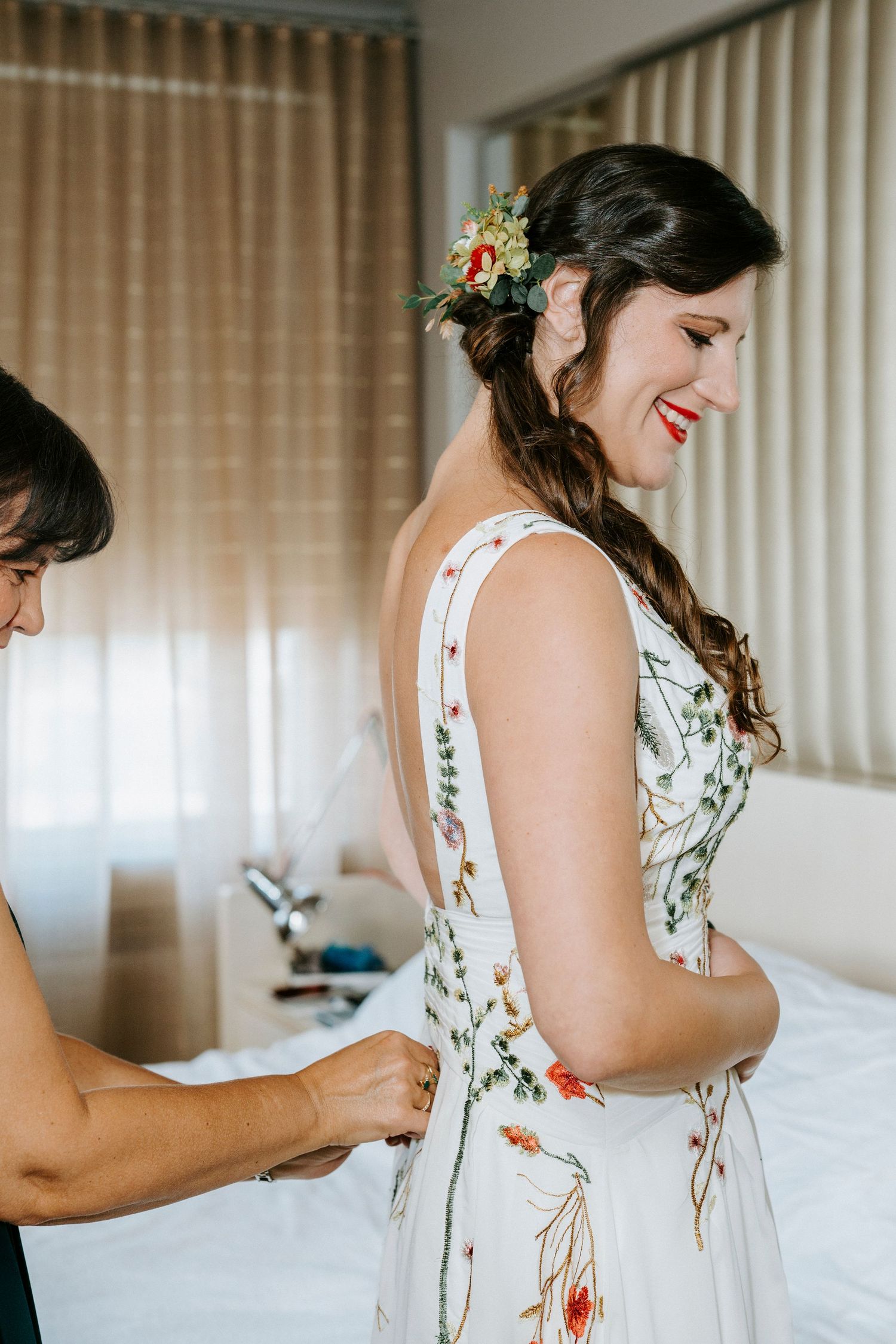 Someone helps zip up a floral white wedding dress on a person getting ready for their special day.