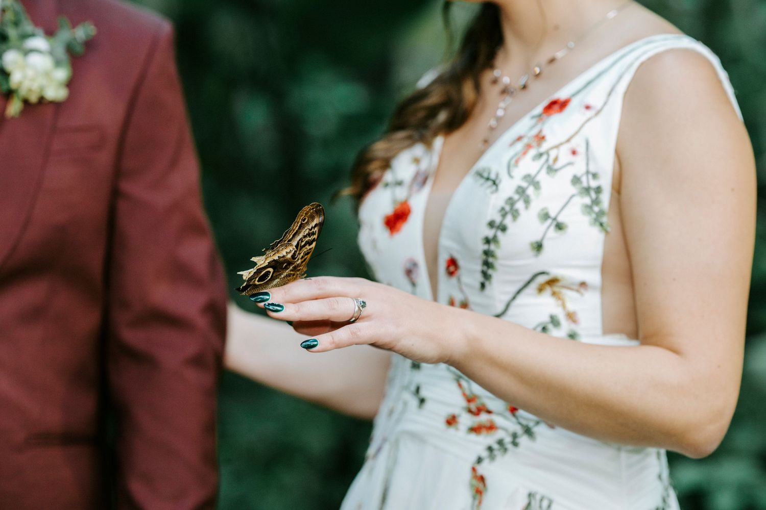 Someone in a white floral dress holds a bouquet during an outdoor ceremony in a forested setting.
