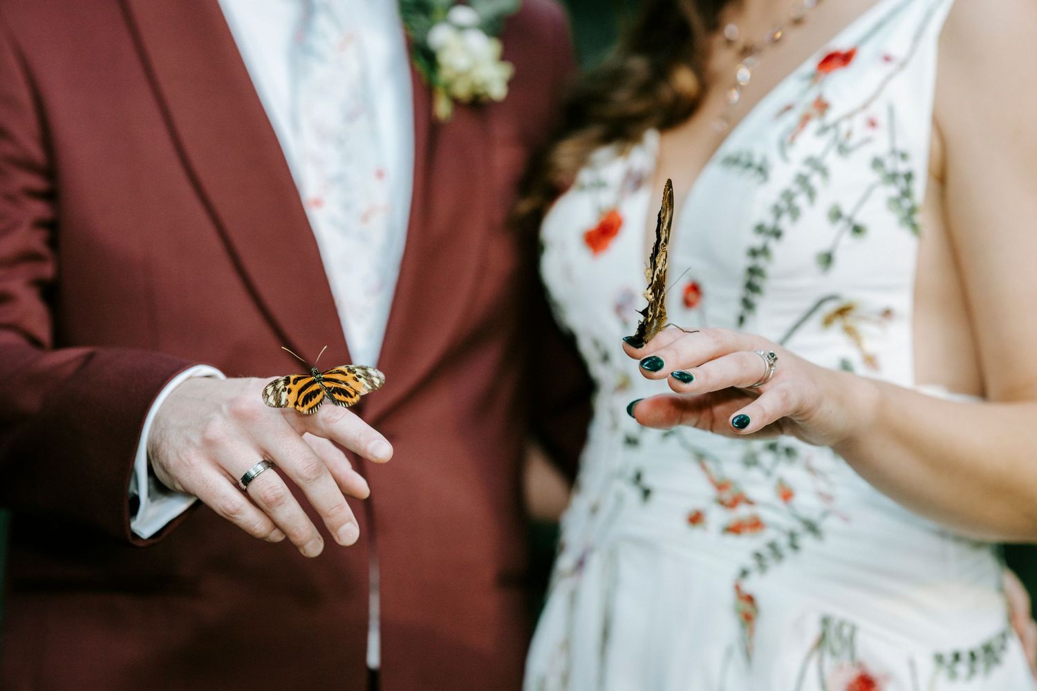 Person wearing burgundy suit jacket next to someone in floral dress during formal event.