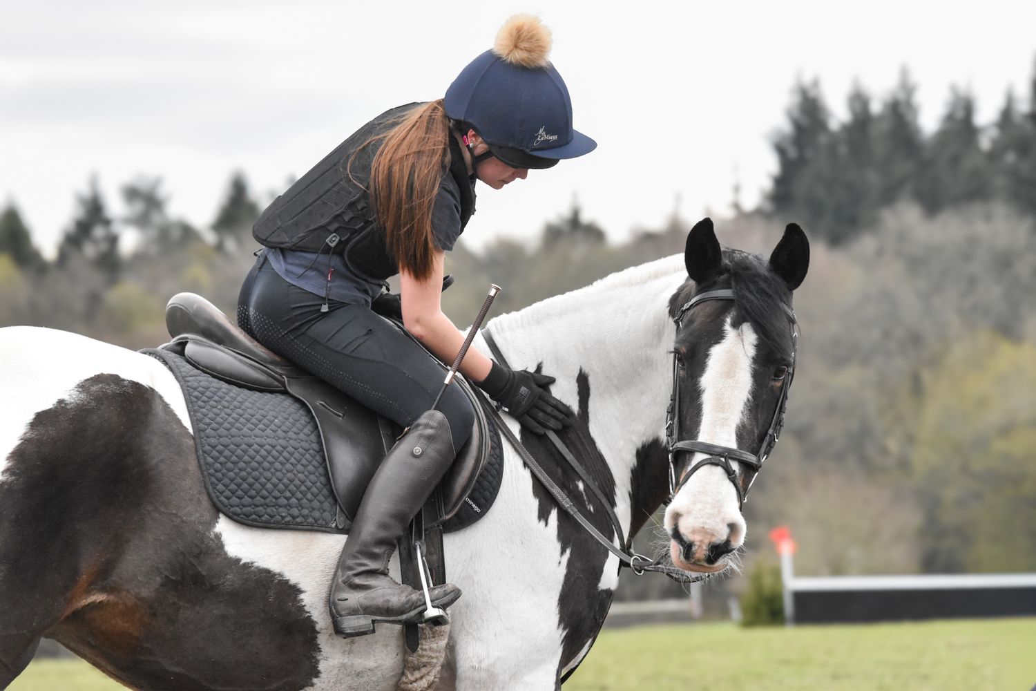 Woman in navy riding hat mounted on a black and white horse during an equestrian competition.