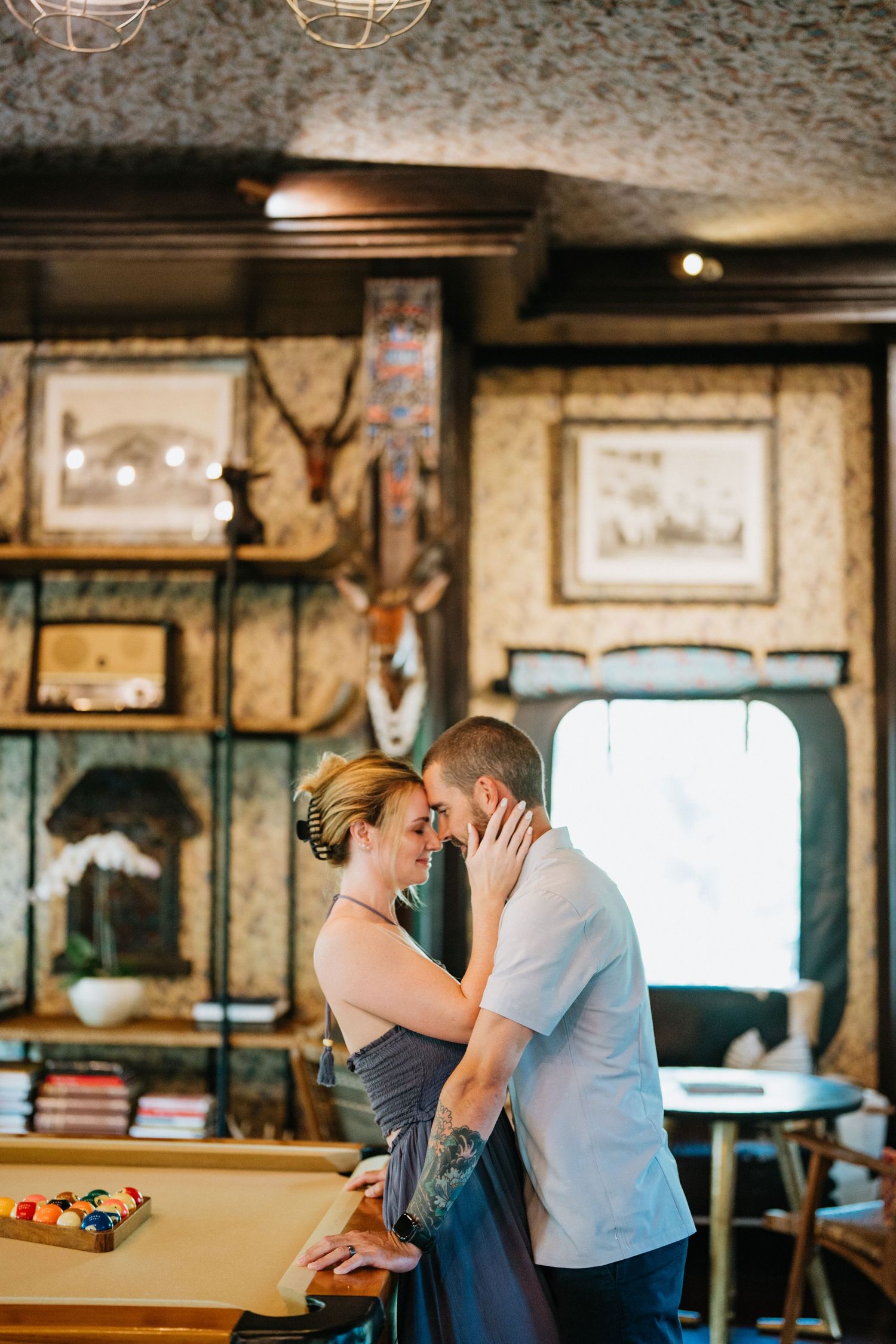 A couple shares a tender moment in a rustic room with vintage decor and warm lighting.