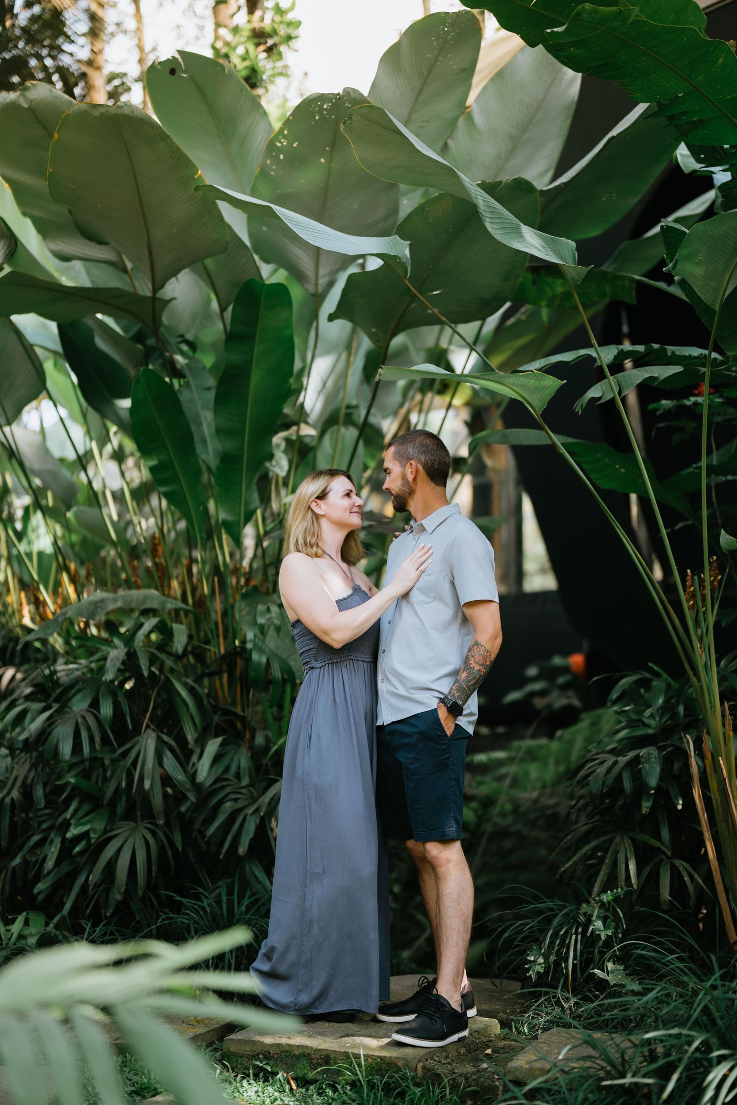 A couple shares an intimate moment among large tropical leaves in a garden setting.