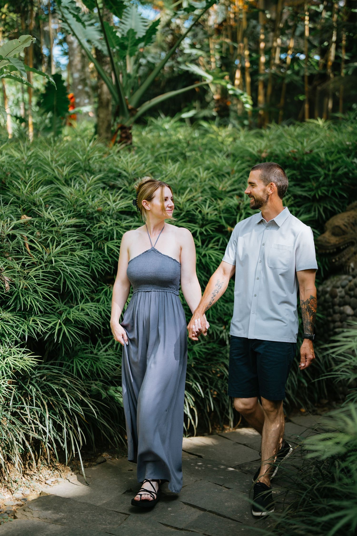Couple walking along garden path surrounded by lush tropical plants and ferns.