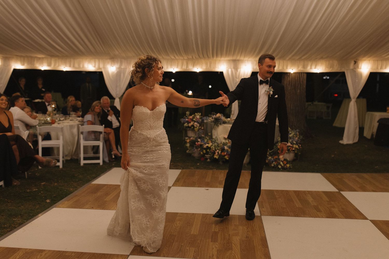 Couple dancing together under white tent at evening wedding reception.