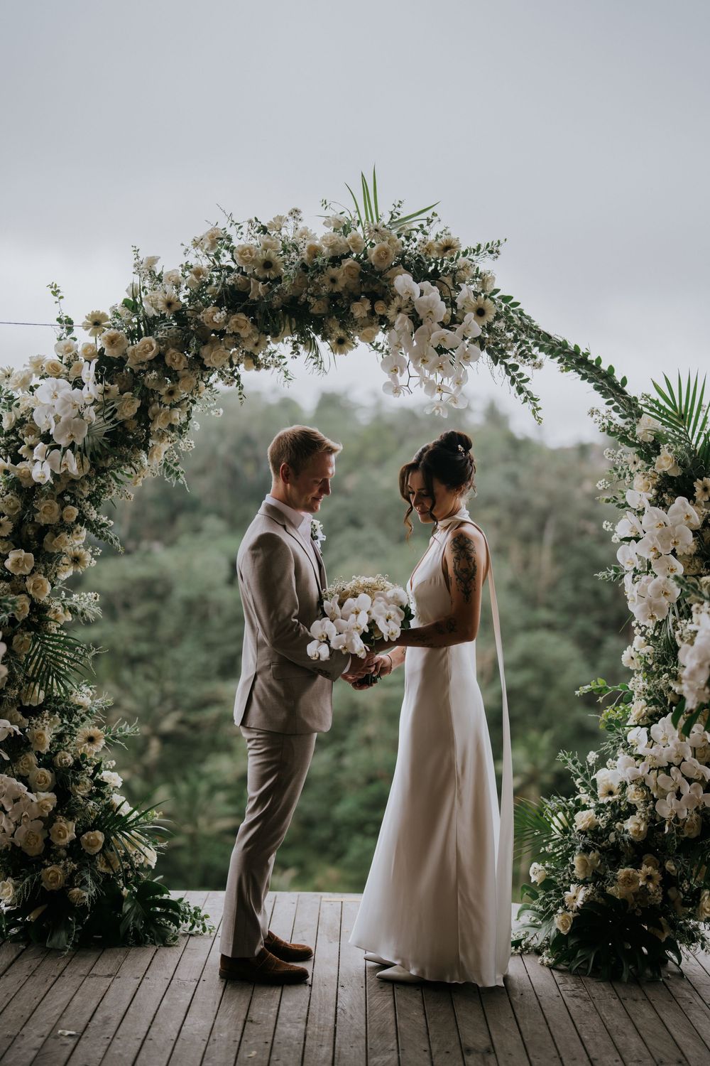 Intimate wedding ceremony under an elegant floral arch with white orchids and roses.