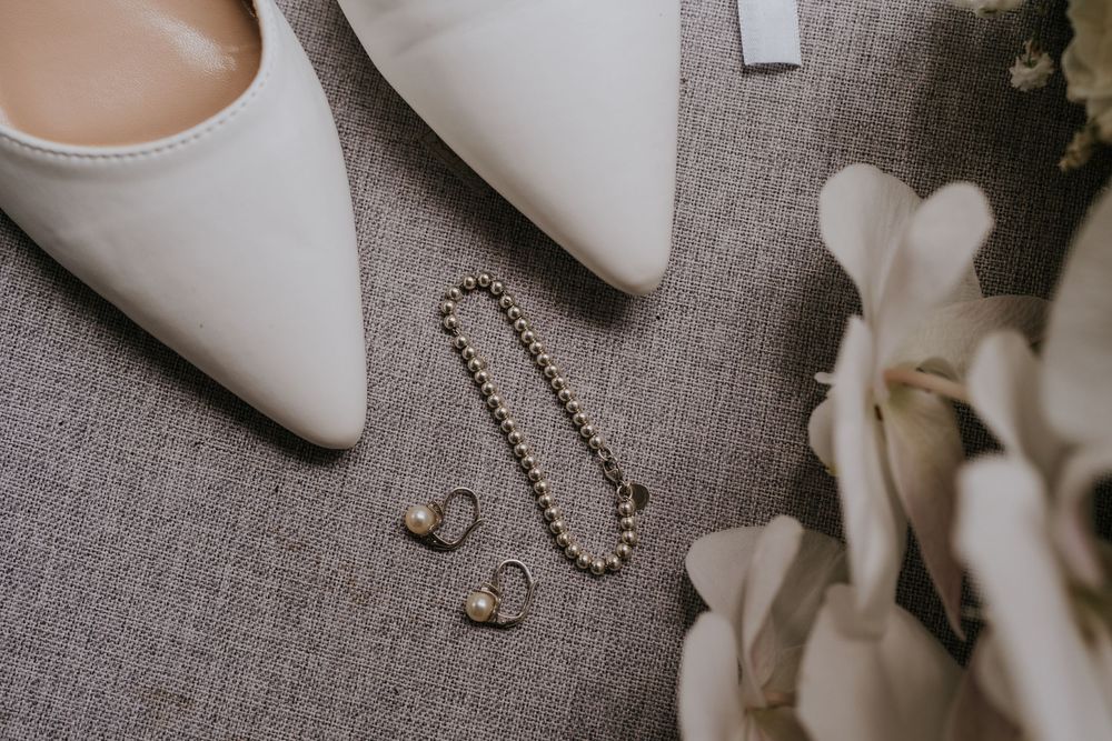Elegant white bridal shoes and pearl accessories arranged on a grey textured background.
