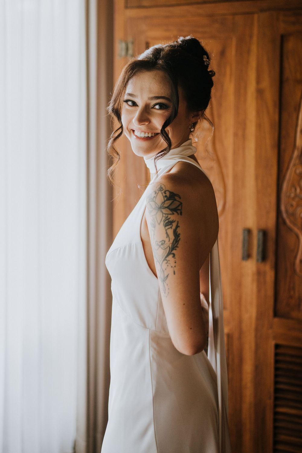 Minimalist white wedding dress shown against wooden wardrobe doors in natural light.