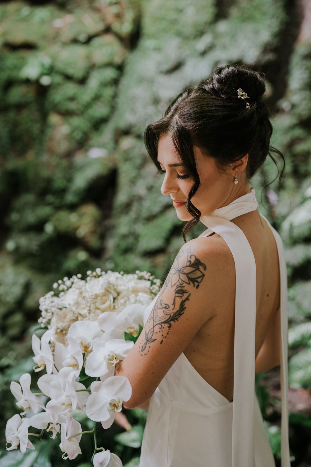 White orchid bouquet and sleek wedding dress photographed against lush green outdoor backdrop.