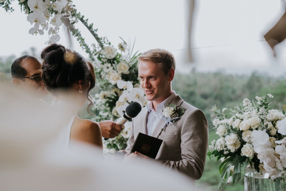 Wedding ceremony under floral arch with white orchids and greenery.