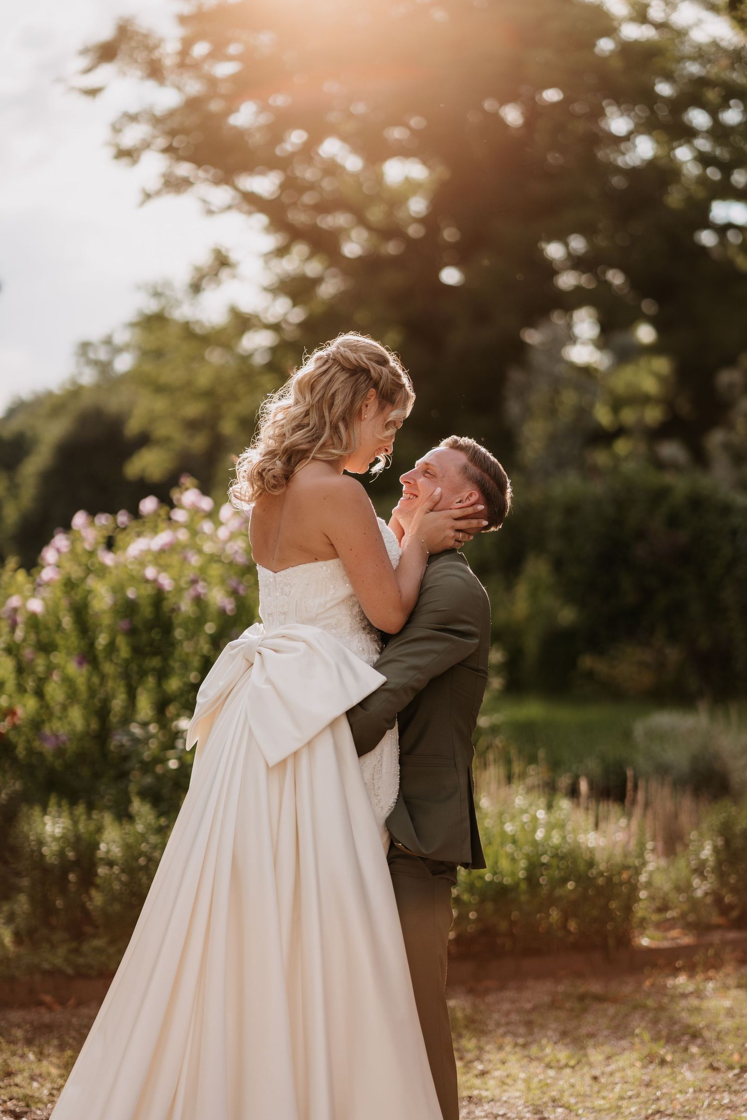 A romantic sunset wedding moment as newlyweds share a kiss in a garden setting with golden light filtering through.
