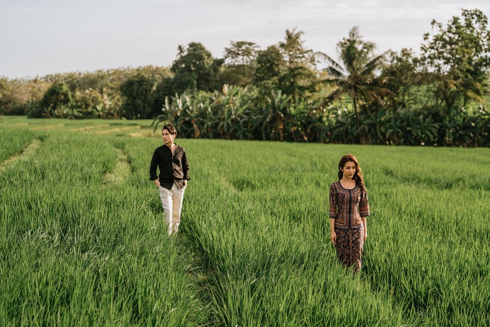 A couple stands apart in a verdant rice field with tropical foliage in the background.