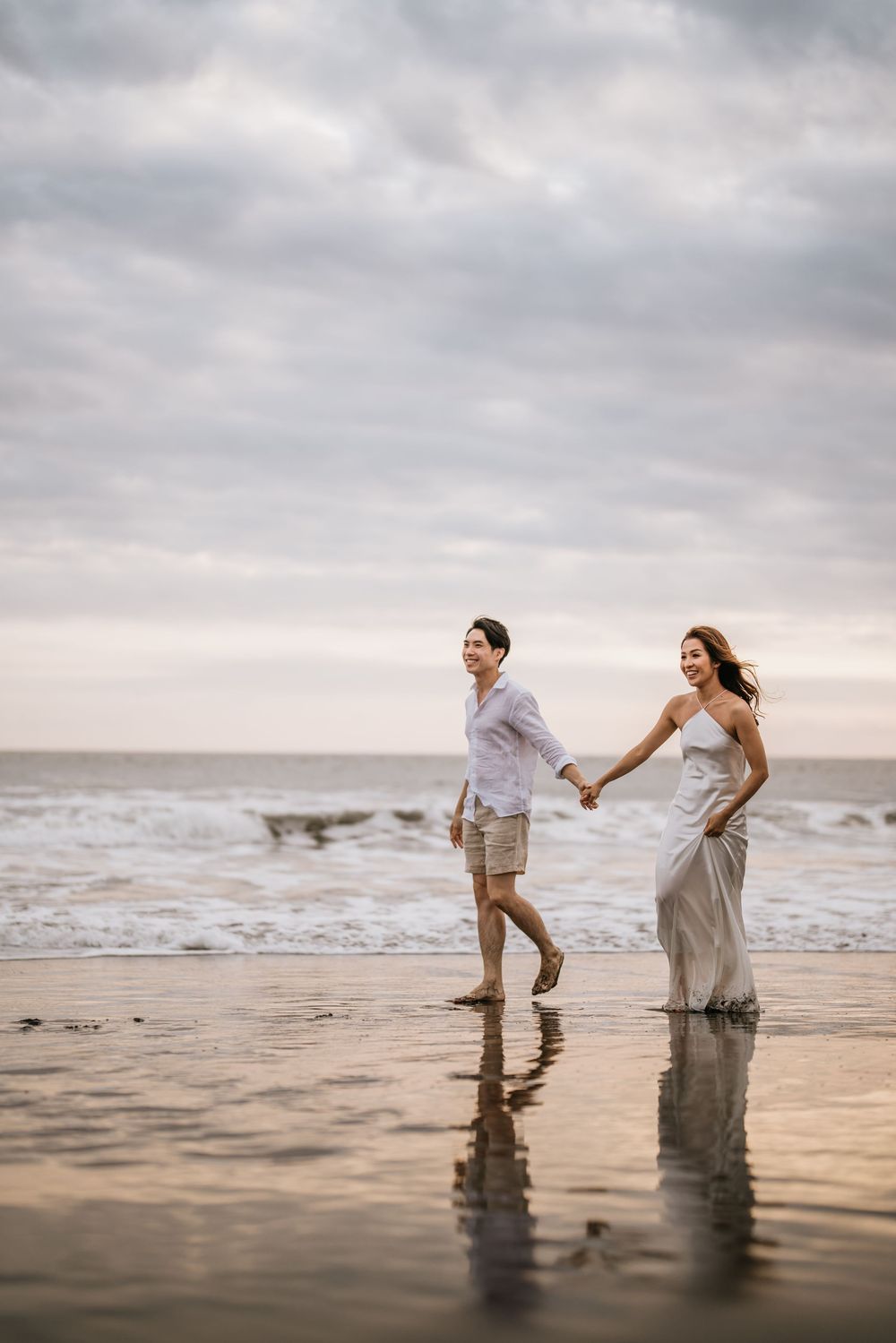 A couple holds hands while dancing in the shallow ocean waves at sunset.