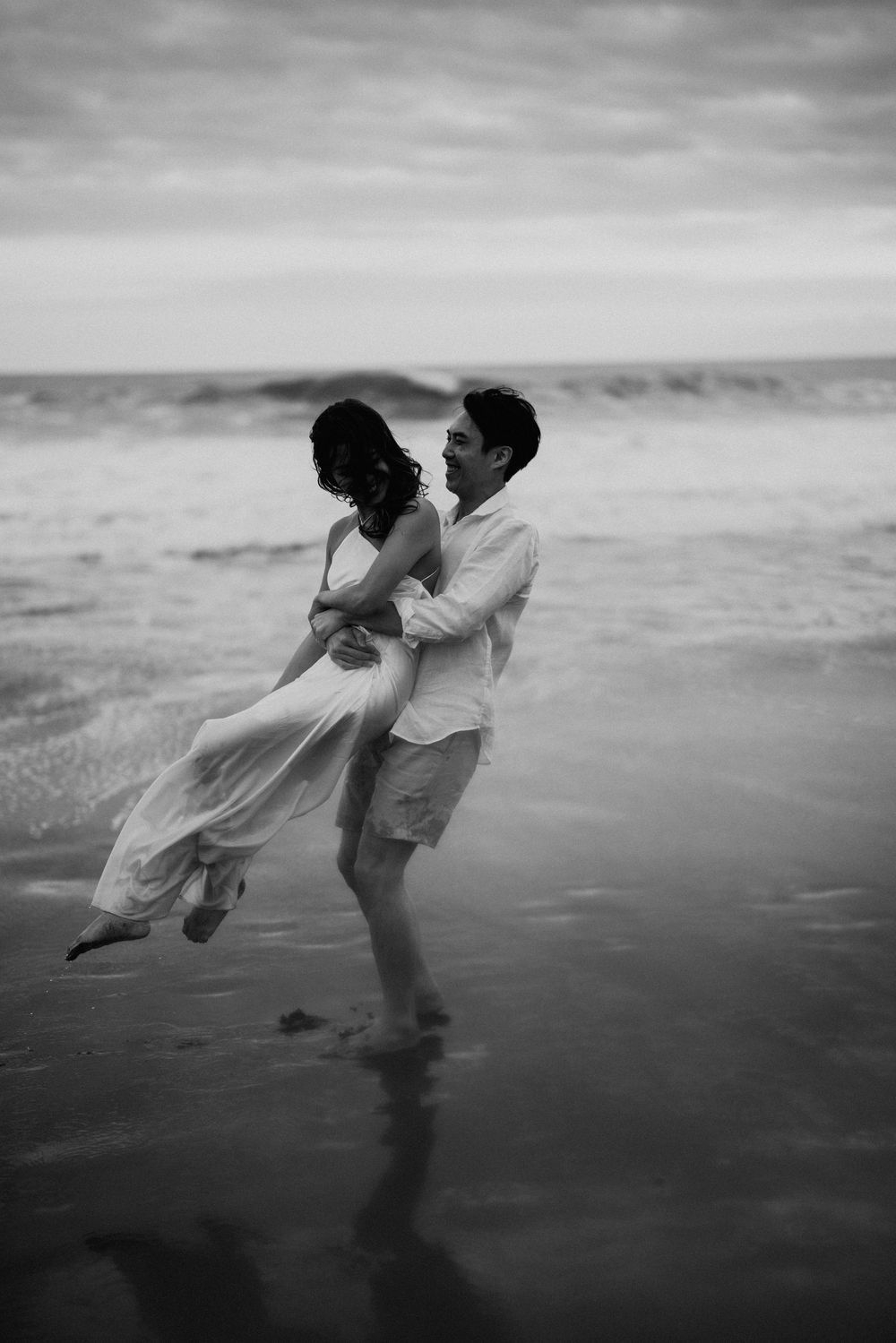 A black and white photo captures a couple dancing on a misty beach.