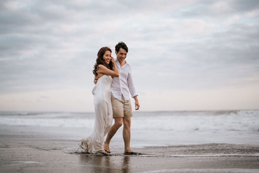 A couple plays in the ocean waves while wearing white clothing at sunset.