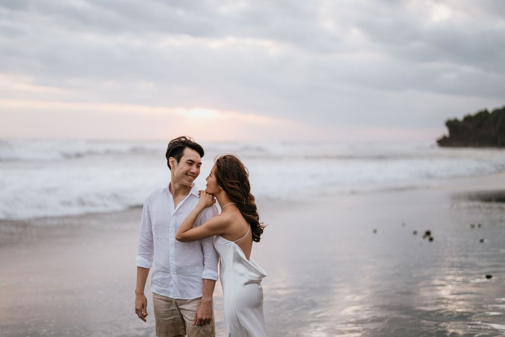 A couple shares a romantic moment while standing in shallow ocean water at dusk.