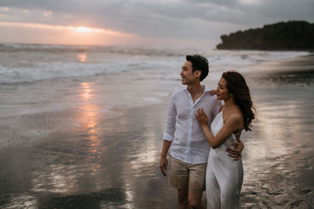 A romantic sunset beach photoshoot with a couple in white attire walking along the shoreline.