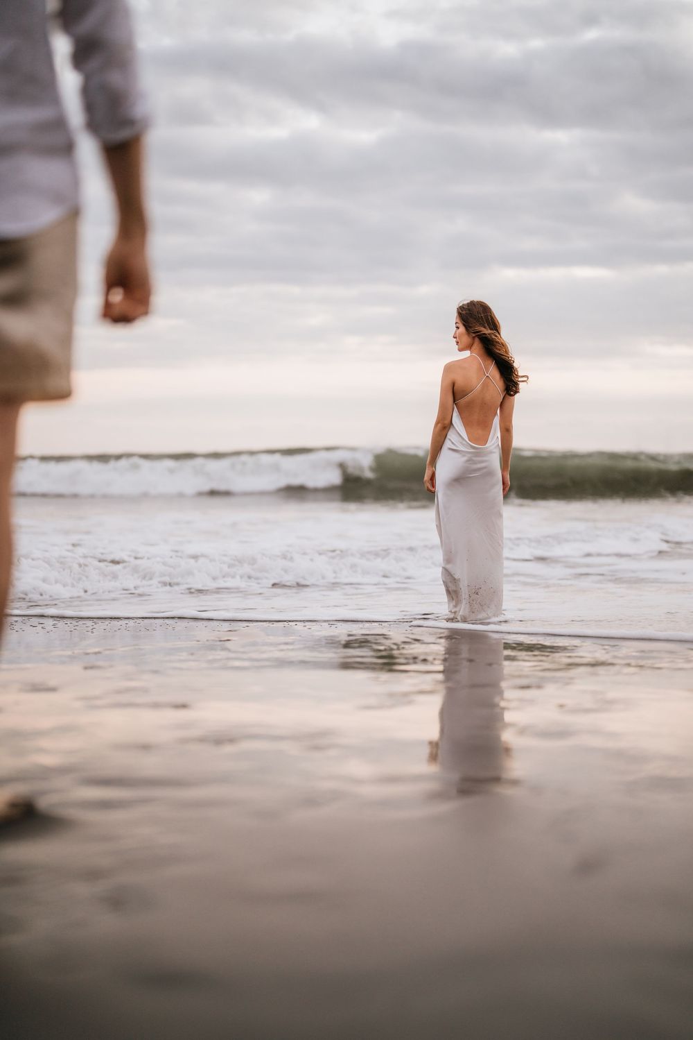 Couple standing in shallow ocean water during golden hour with soft waves rolling in.