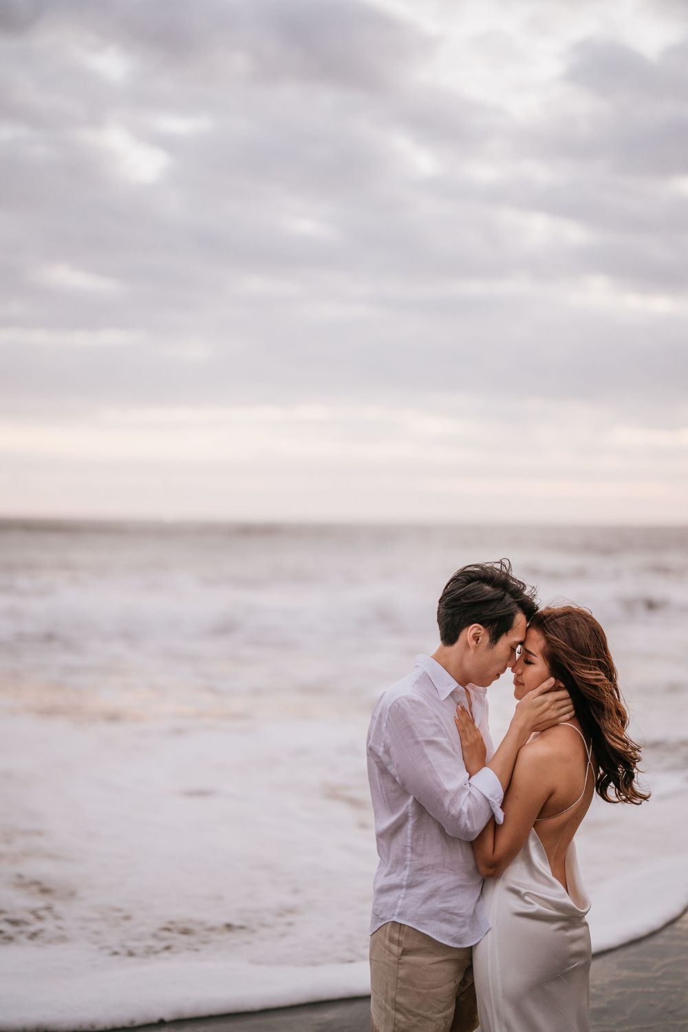 Intimate beach portraits at sunset with couple in white and beige attire.