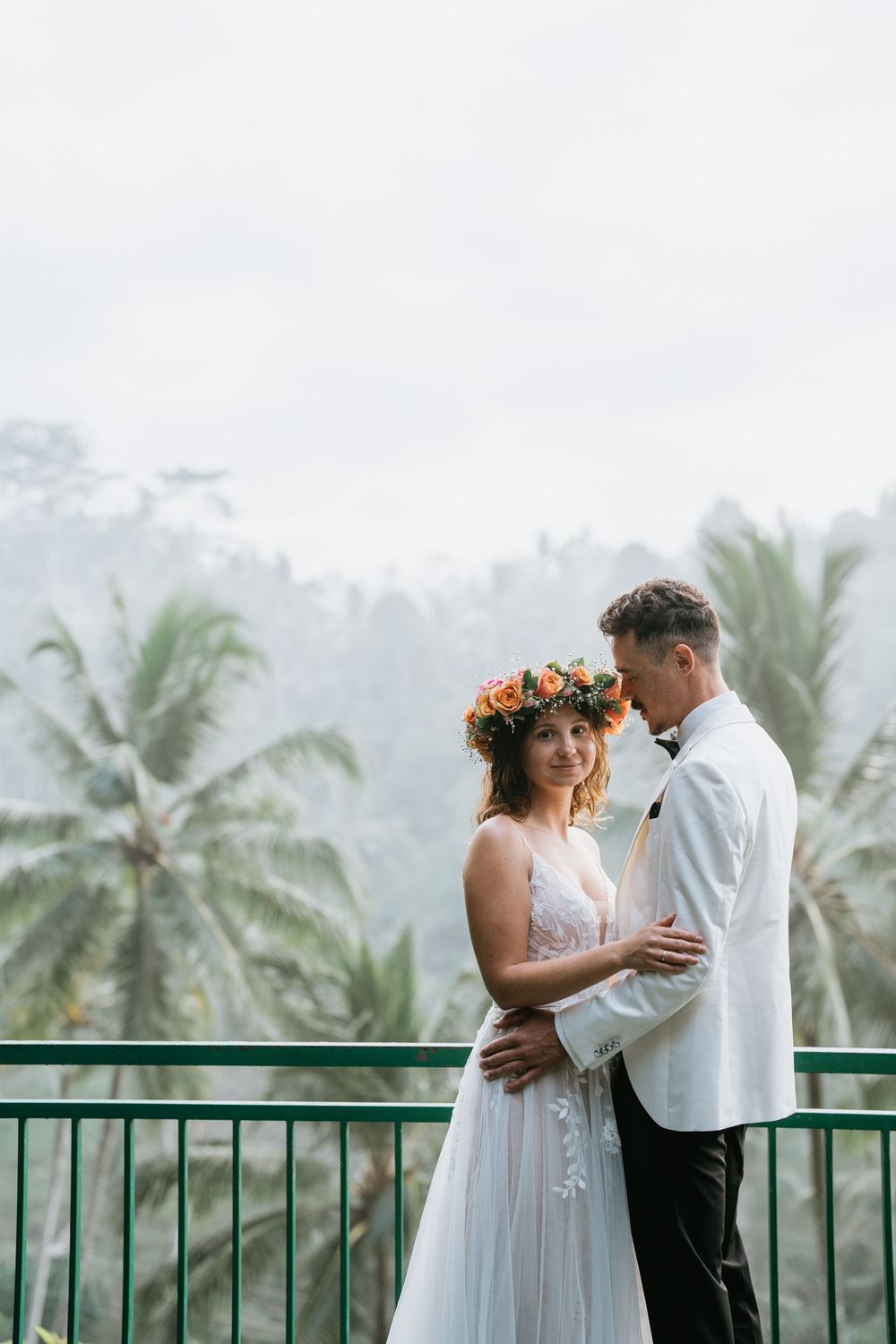 Tender embrace on a viewing deck surrounded by swaying palm trees in a tropical setting.