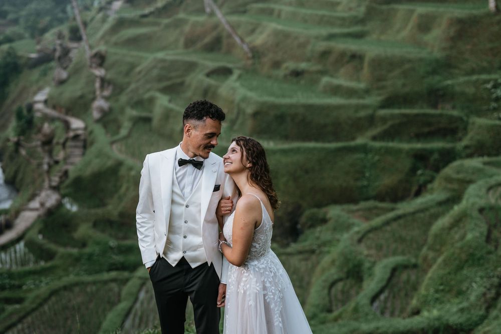 Couple poses on stone steps amid terraced rice paddies in Bali.