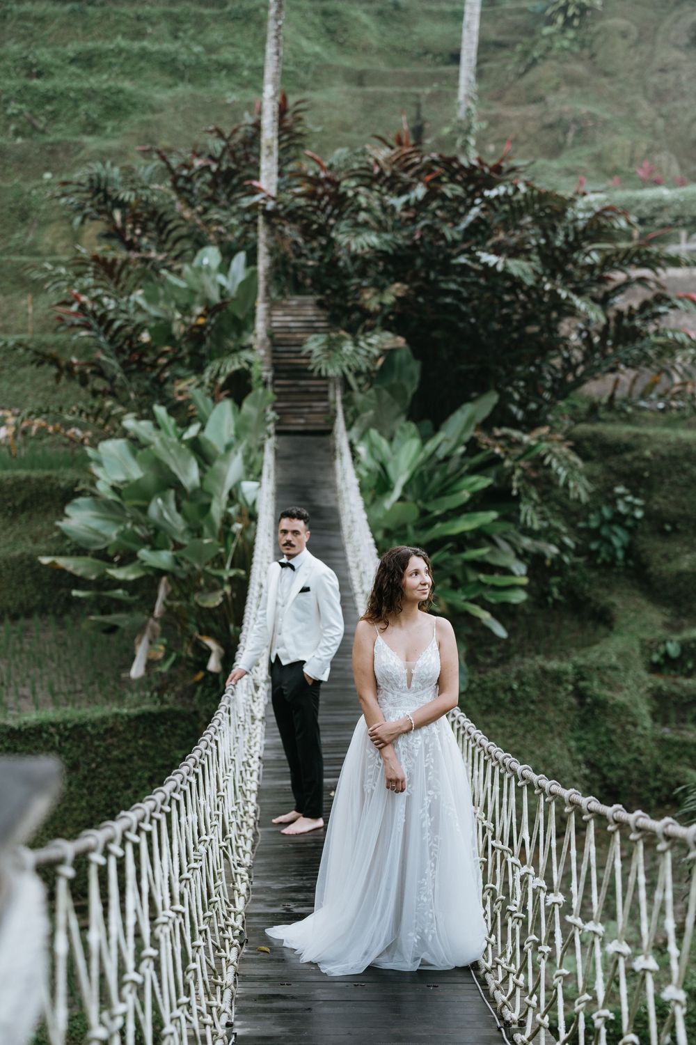Romantic moment on a rope bridge surrounded by tropical foliage and palm trees.