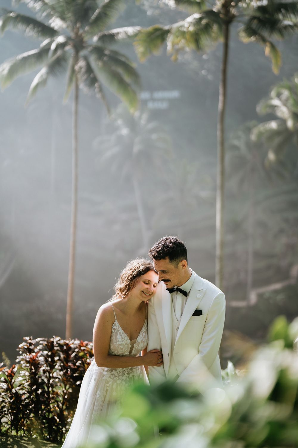 Intimate wedding portrait with soft sunlight filtering through tropical palm trees.