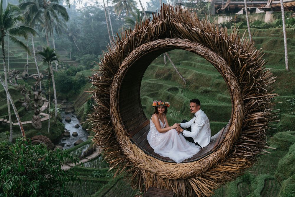 Wedding photos in a giant woven nest structure surrounded by palm trees and tropical scenery.