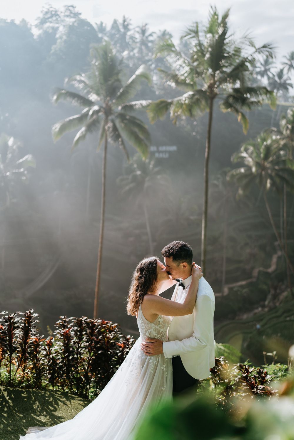 Romantic wedding photoshoot with palm trees and sunlight creating a dreamy tropical atmosphere.
