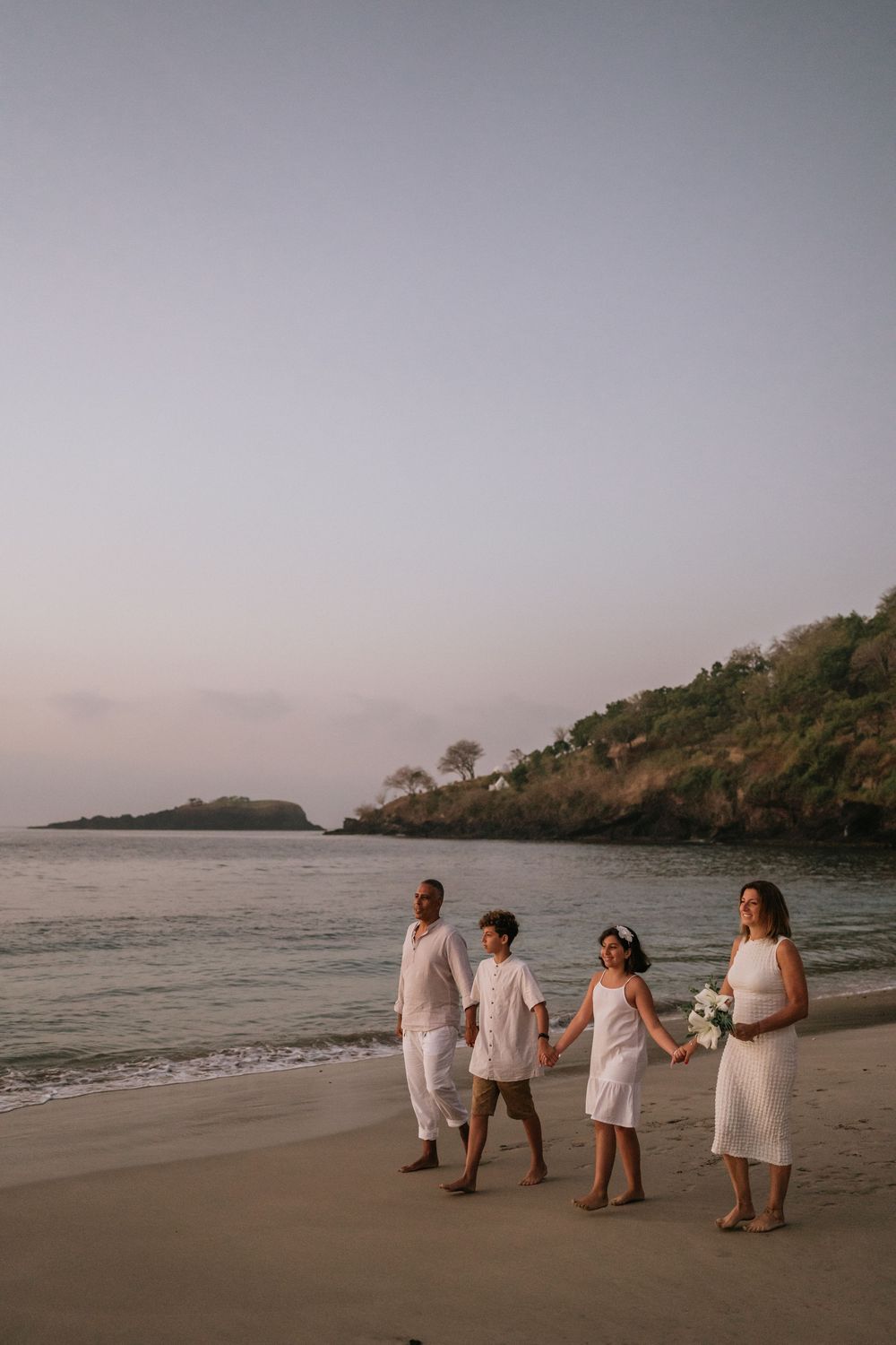 Group walking together on beach at dusk with rocky coastline in background.