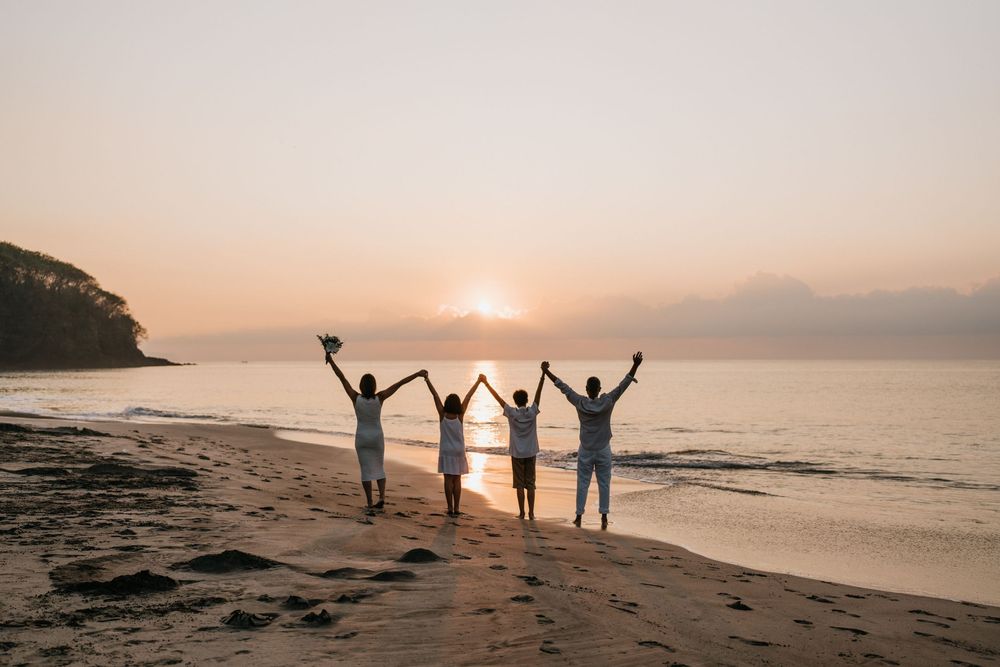 People raising arms in celebration at sunset on beach with ocean waves behind them.