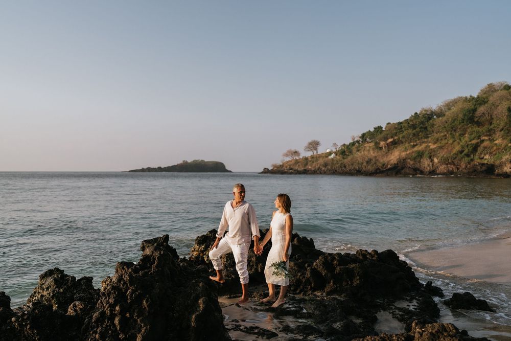 Family members walking along rocky coastal beach in coordinated white outfits.