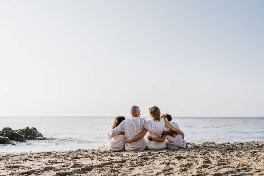 Group sitting close together on beach shoreline while watching the ocean view.
