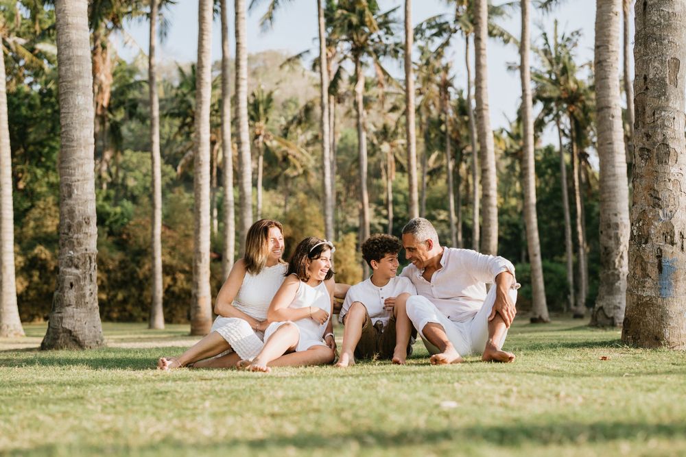 Family relaxing on grass under tall palm trees in a tropical setting.