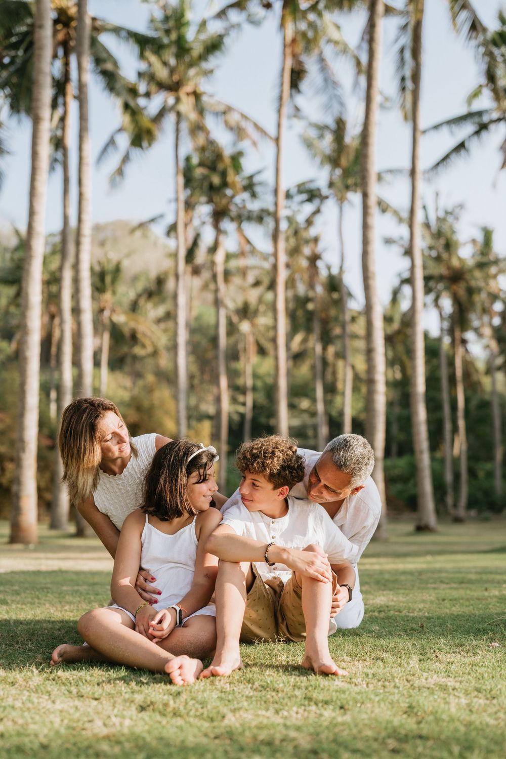 Family laying together on grass under palm trees sharing intimate moments.