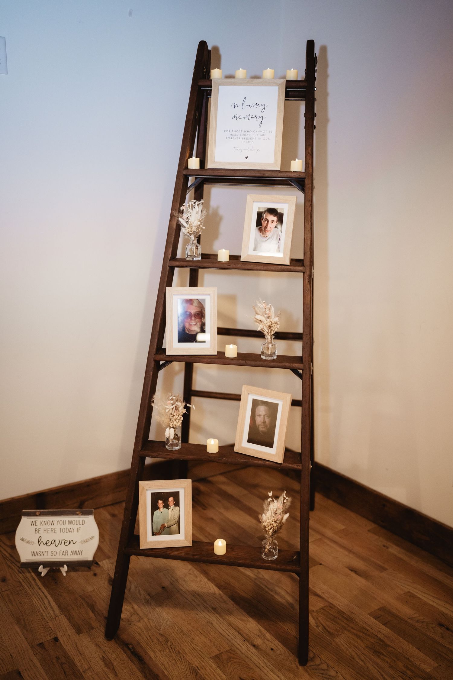 Dark wooden ladder shelf with photographs and decorative items displayed on hardwood flooring creates memorial display.