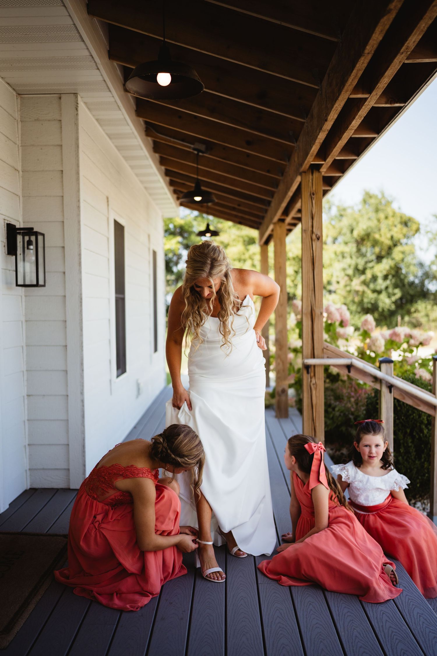 A sequence of playful bridal party photos showing bridesmaids in coral dresses peeking around corners of a white porch.