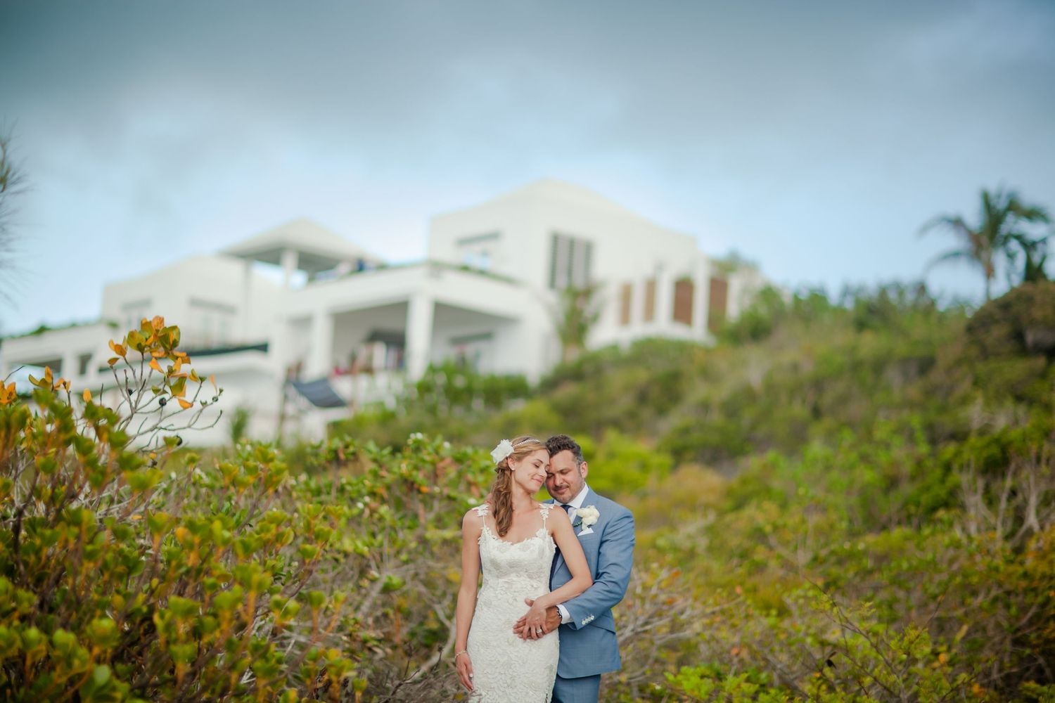 Couple embracing in front of a modern coastal home surrounded by lush greenery.