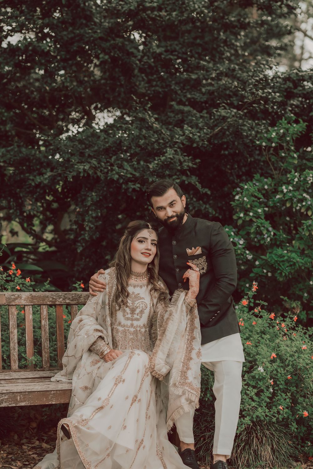 Couple sharing tender romantic moments while sitting on wooden bench in a lush garden setting.