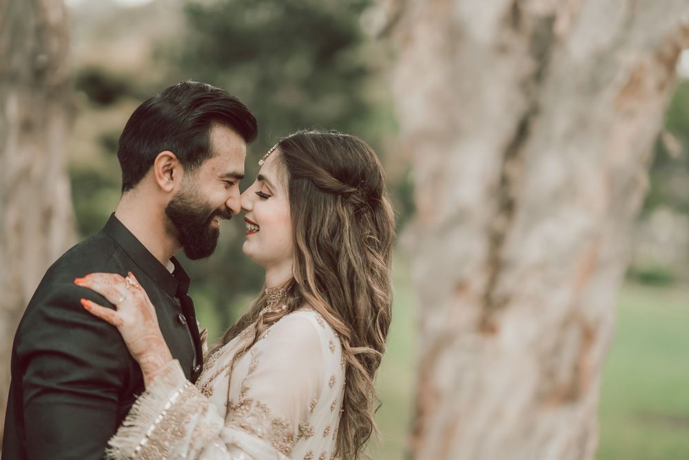 A romantic couple shares an intimate moment outdoors with soft lighting near a tree trunk.