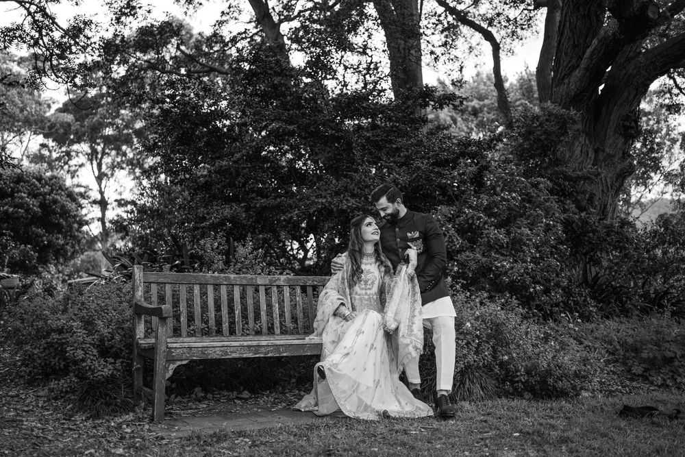 A couple poses for romantic outdoor wedding photos in black and white surrounded by lush gardens and trees.