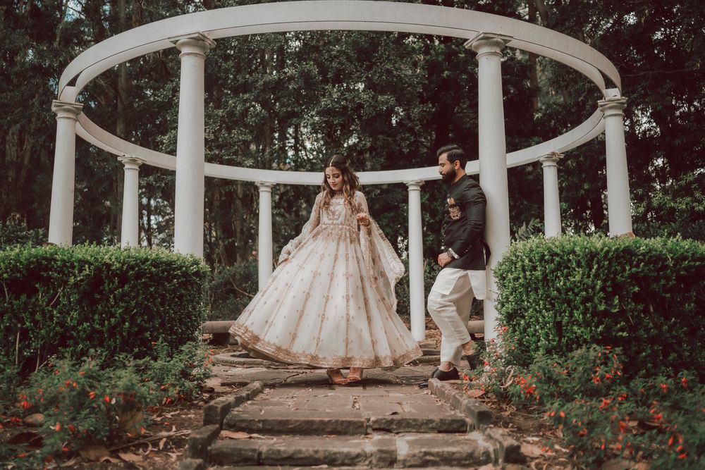 A flowing white wedding dress hangs on an ornate white garden arbor surrounded by lush greenery and roses.