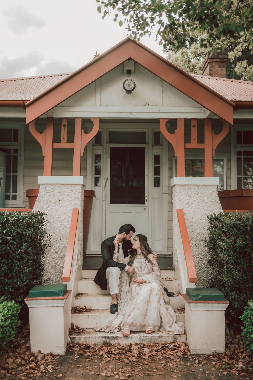 A romantic scene on the steps of a charming craftsman bungalow with peach-colored trim and white stone columns.