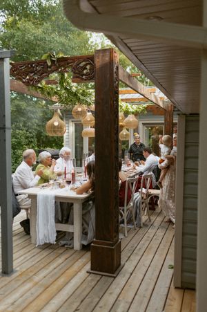 Guests seated at long tables on a wooden deck for an outdoor dinner party.
