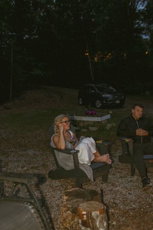 People relaxing in camping chairs at dusk with a car visible in the background.