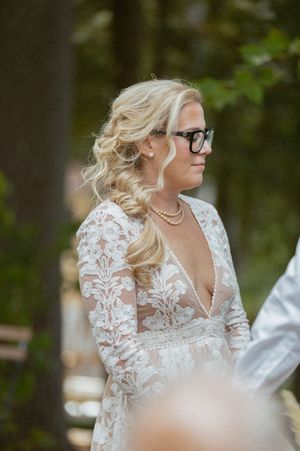 Side profile of a bride in a lace wedding dress with glasses outdoors.
