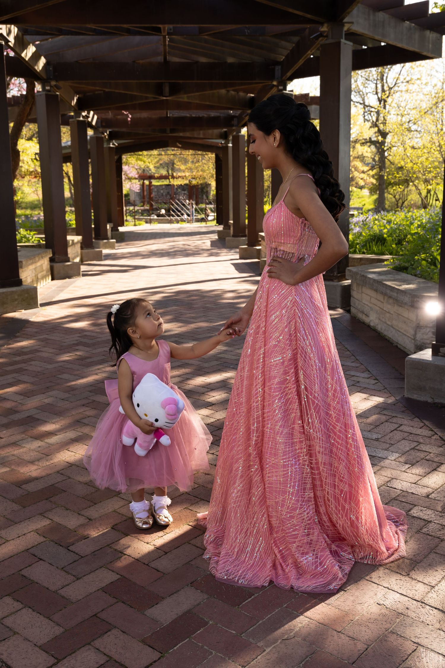 Sweet 16 girl in a pink ballgown walking with a toddler in a garden. Professional lifestyle and event photography by Alex T.