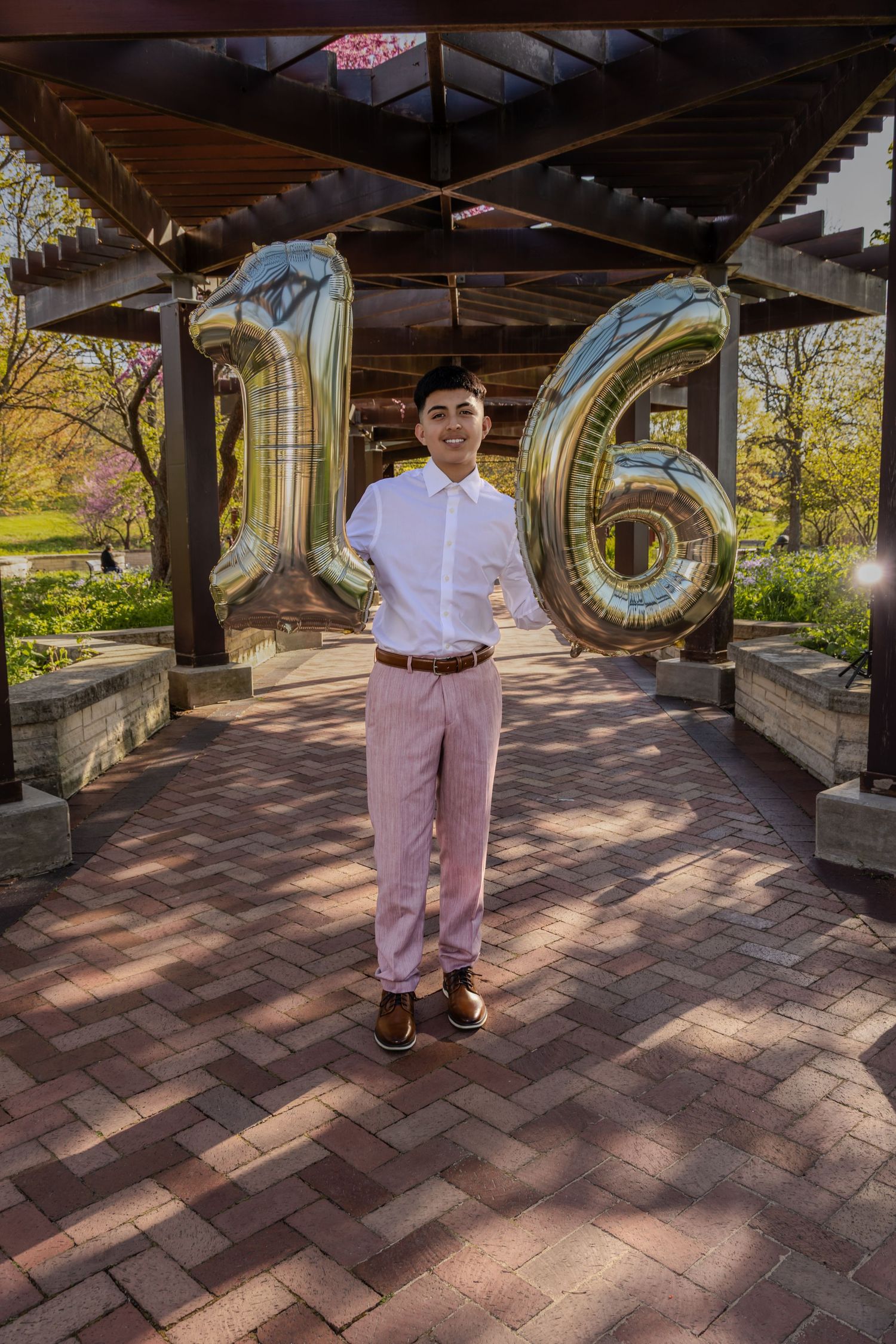 Sweet 16 boy posing with large gold "16" balloons in a garden. Modern Sweet 16 celebration photography in Waukegan by Alex T.