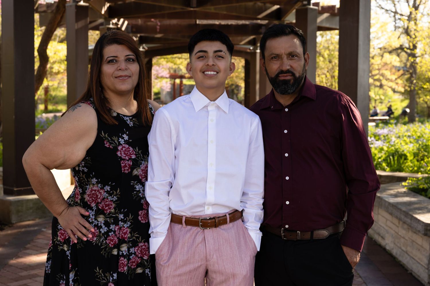Heartfelt family portrait of a Quinceañera with her parents in a sun-drenched park. Expert Lake County family photography by Alex T.